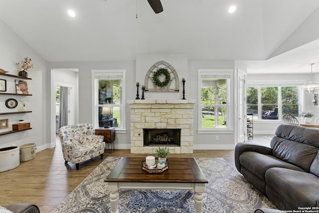 living area with vaulted ceiling, wood finished floors, a stone fireplace, and a ceiling fan