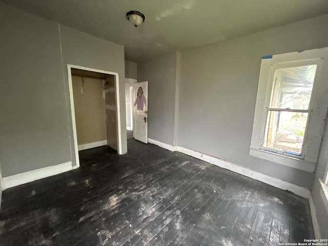 unfurnished bedroom featuring baseboards, a closet, and dark wood-style flooring