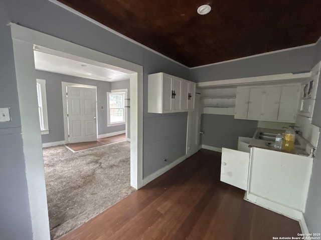 kitchen featuring dark wood-type flooring, baseboards, a sink, and white cabinetry
