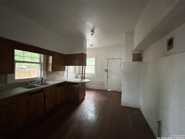 kitchen featuring a peninsula, dark wood-style floors, a sink, brown cabinetry, and light countertops