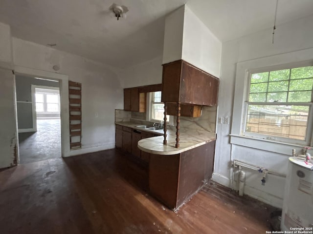 kitchen featuring a sink, water heater, light countertops, a peninsula, and dark wood-style flooring