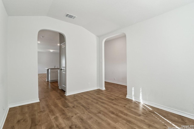 unfurnished room with wood finished floors, visible vents, and arched walkways