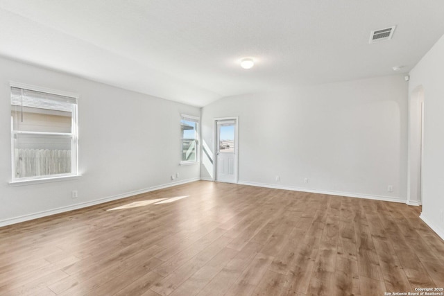 spare room featuring light wood-type flooring, visible vents, lofted ceiling, and baseboards
