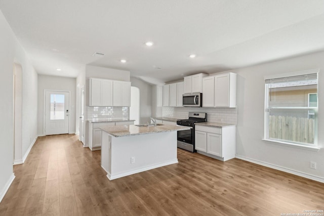 kitchen with decorative backsplash, appliances with stainless steel finishes, a sink, and a kitchen island with sink