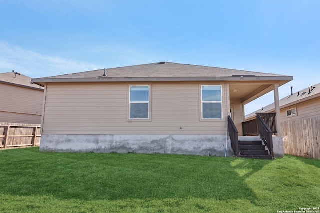 rear view of house featuring fence and a lawn