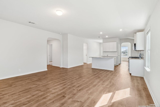 unfurnished living room with recessed lighting, visible vents, arched walkways, and light wood-style floors