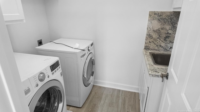 clothes washing area with cabinet space, a sink, light wood finished floors, baseboards, and washing machine and dryer