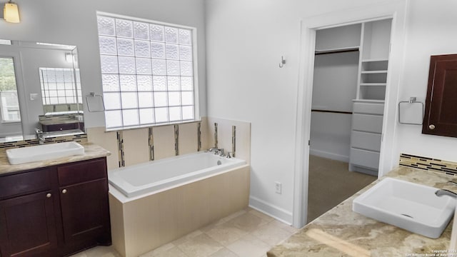 bathroom with a walk in closet, two vanities, a sink, and a bath