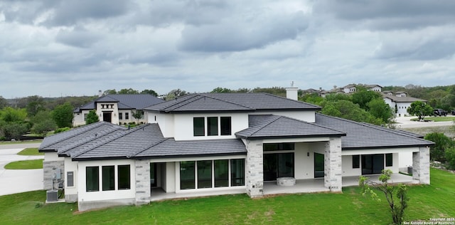 back of property featuring a chimney, a lawn, a patio area, cooling unit, and stucco siding