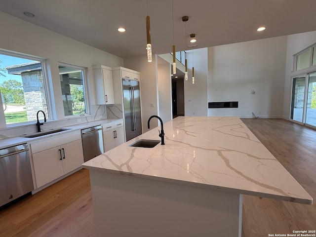 kitchen featuring a kitchen island with sink, appliances with stainless steel finishes, a sink, and light wood-type flooring