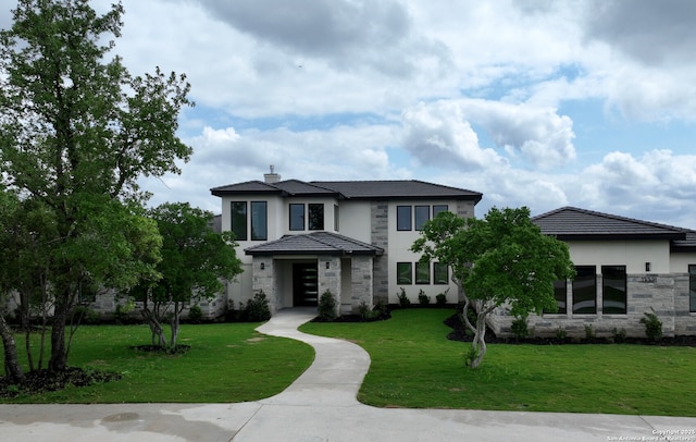 prairie-style home featuring a chimney, stucco siding, a front yard, and stone siding