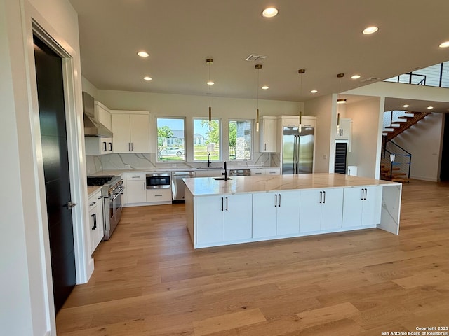 kitchen featuring a spacious island, high quality appliances, white cabinetry, wall chimney exhaust hood, and backsplash