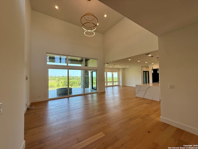 unfurnished living room featuring baseboards, a chandelier, light wood finished floors, and a towering ceiling