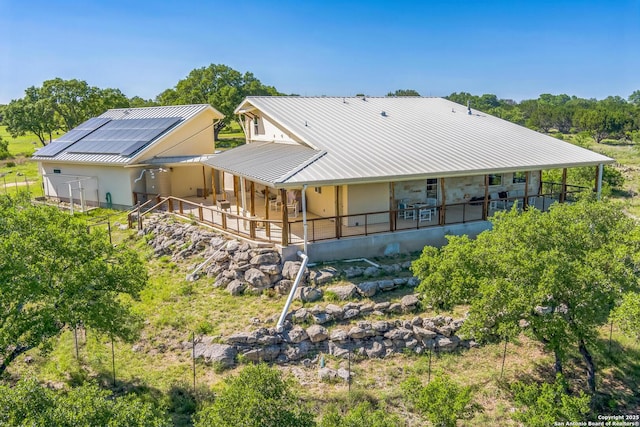 rear view of house featuring stucco siding, roof mounted solar panels, and metal roof