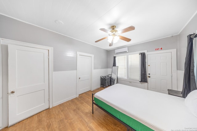 bedroom featuring ceiling fan, a wainscoted wall, wood finished floors, and a wall unit AC
