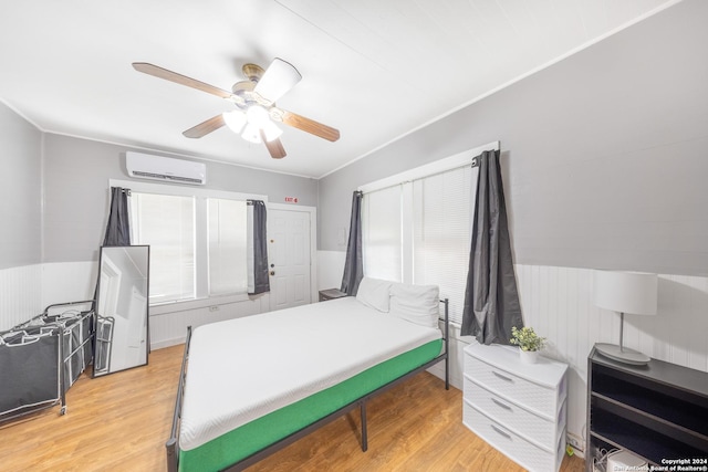 bedroom featuring ceiling fan, a wainscoted wall, light wood-style floors, and a wall unit AC
