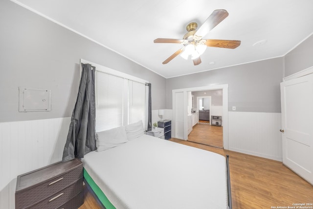 bedroom with light wood-type flooring, a wainscoted wall, and ceiling fan