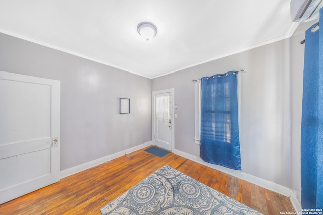 entryway featuring baseboards, hardwood / wood-style flooring, ornamental molding, and a wall unit AC