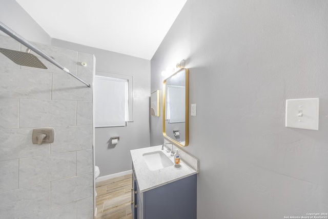 full bath featuring a tile shower, wood finished floors, toilet, vanity, and baseboards