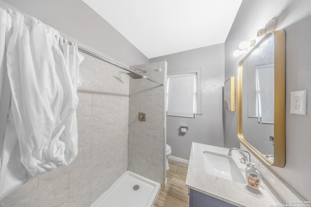 bathroom with wood finished floors, toilet, vanity, baseboards, and tiled shower