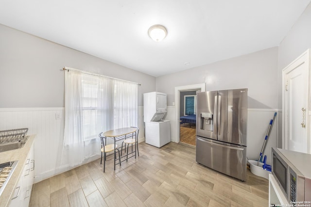 kitchen featuring wainscoting, stainless steel appliances, stacked washing maching and dryer, and light countertops