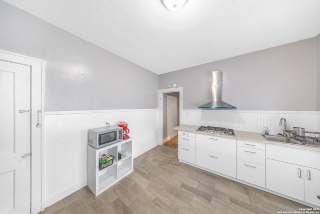 kitchen featuring wall chimney range hood, a wainscoted wall, light countertops, white cabinets, and appliances with stainless steel finishes