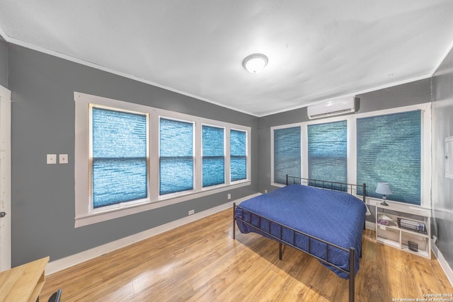 bedroom with an AC wall unit, baseboards, crown molding, and wood finished floors