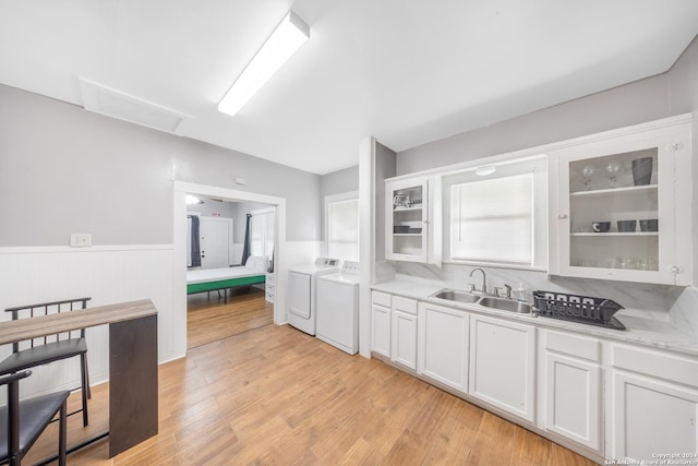 kitchen featuring a sink, washing machine and dryer, wainscoting, glass insert cabinets, and light countertops