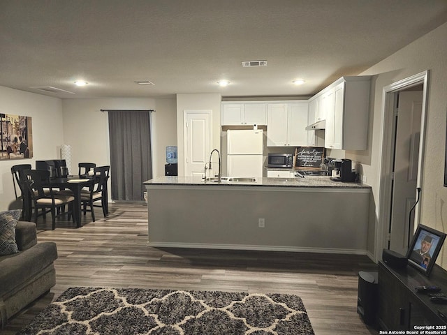 kitchen with dark wood-style floors, a sink, stainless steel microwave, visible vents, and freestanding refrigerator