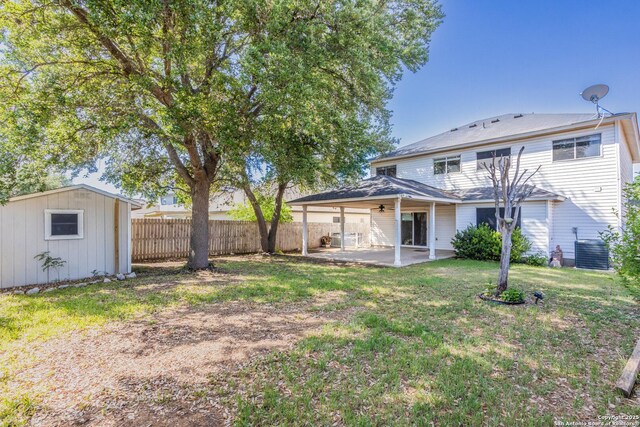 back of property with a patio area, an outdoor structure, fence, a yard, and ceiling fan