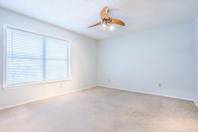 spare room featuring ceiling fan, light carpet, a textured ceiling, and baseboards