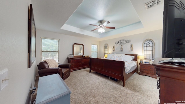 bedroom featuring a raised ceiling, visible vents, light colored carpet, and ceiling fan