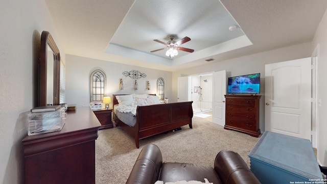 carpeted bedroom with a ceiling fan, a tray ceiling, and visible vents