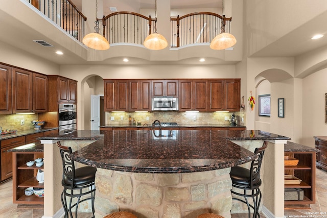 kitchen with arched walkways, stainless steel appliances, open shelves, a large island, and a towering ceiling