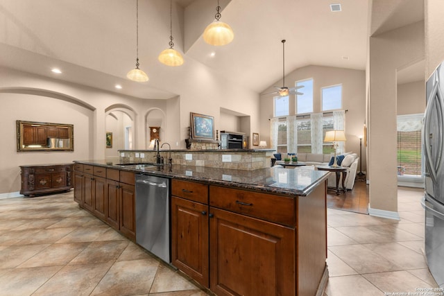 kitchen with a sink, stainless steel appliances, arched walkways, open floor plan, and a center island with sink