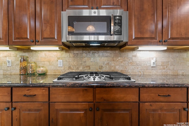 kitchen featuring tasteful backsplash, brown cabinets, appliances with stainless steel finishes, and dark stone counters