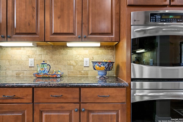kitchen with dark stone countertops, brown cabinetry, backsplash, and double oven