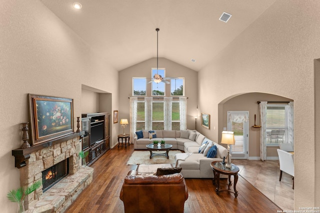 living area with arched walkways, hardwood / wood-style flooring, ceiling fan, a fireplace, and high vaulted ceiling