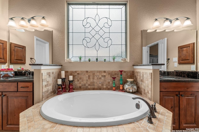 bathroom featuring two vanities, a garden tub, and a sink