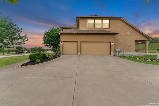 view of front of home with stucco siding, roof with shingles, driveway, and a garage