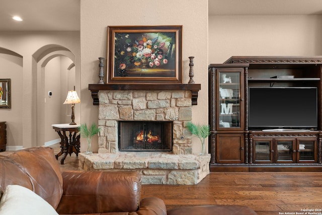 living area featuring wood finished floors, recessed lighting, a stone fireplace, and baseboards