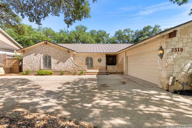 single story home featuring concrete driveway, an attached garage, stone siding, and metal roof