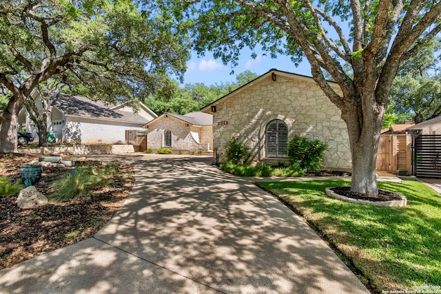 view of front of house with a gate, stone siding, concrete driveway, and fence