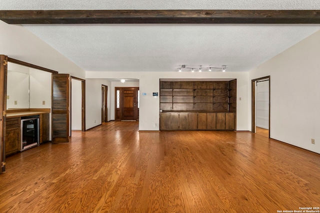 unfurnished living room featuring a textured ceiling, wood finished floors, beam ceiling, and wine cooler