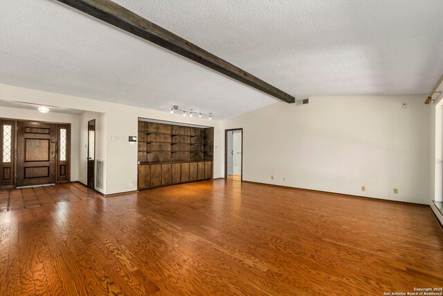 unfurnished living room featuring baseboards, vaulted ceiling with beams, wood finished floors, and a textured ceiling