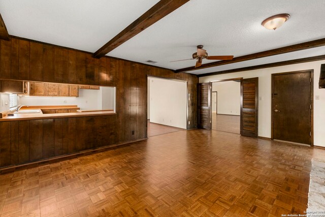 unfurnished living room with beam ceiling, visible vents, baseboards, wood walls, and ceiling fan