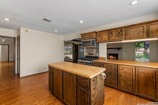 kitchen with a stone fireplace, light wood-type flooring, butcher block counters, appliances with stainless steel finishes, and visible vents