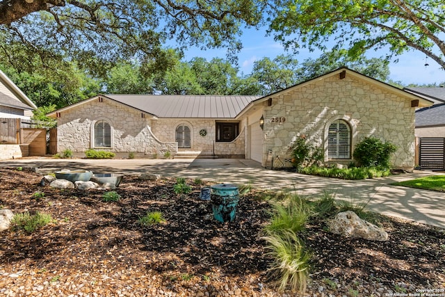 ranch-style house with metal roof, an attached garage, stone siding, and concrete driveway