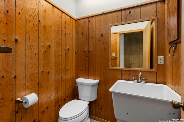half bathroom featuring toilet, a sink, and wooden walls