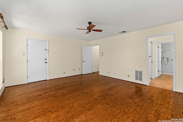 empty room featuring wood finished floors, a ceiling fan, visible vents, and a textured ceiling
